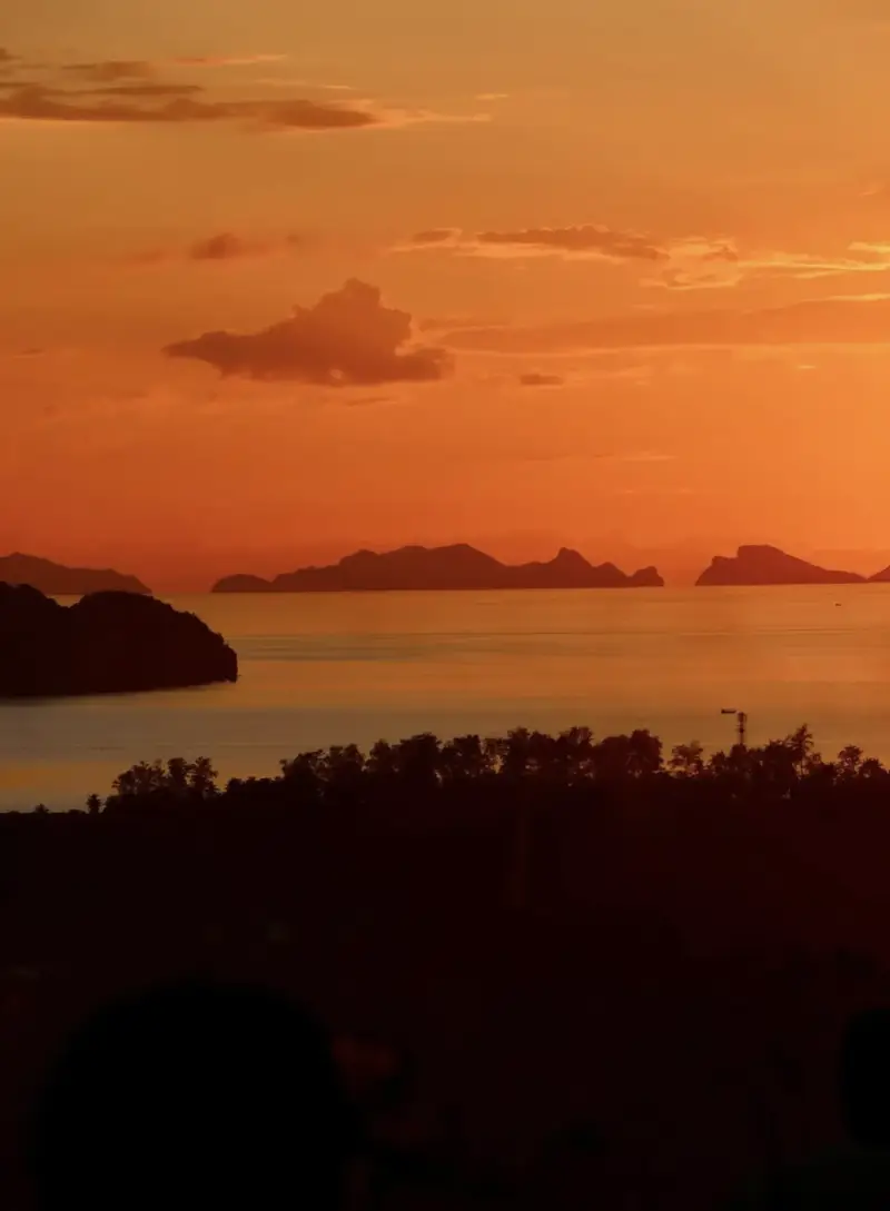 Deep orange sunset over the Gulf of Thailand seen from Secret Mountain, Koh Phangan, with the Ang Thong islands silhouetted on the horizon above the jungle canopy
